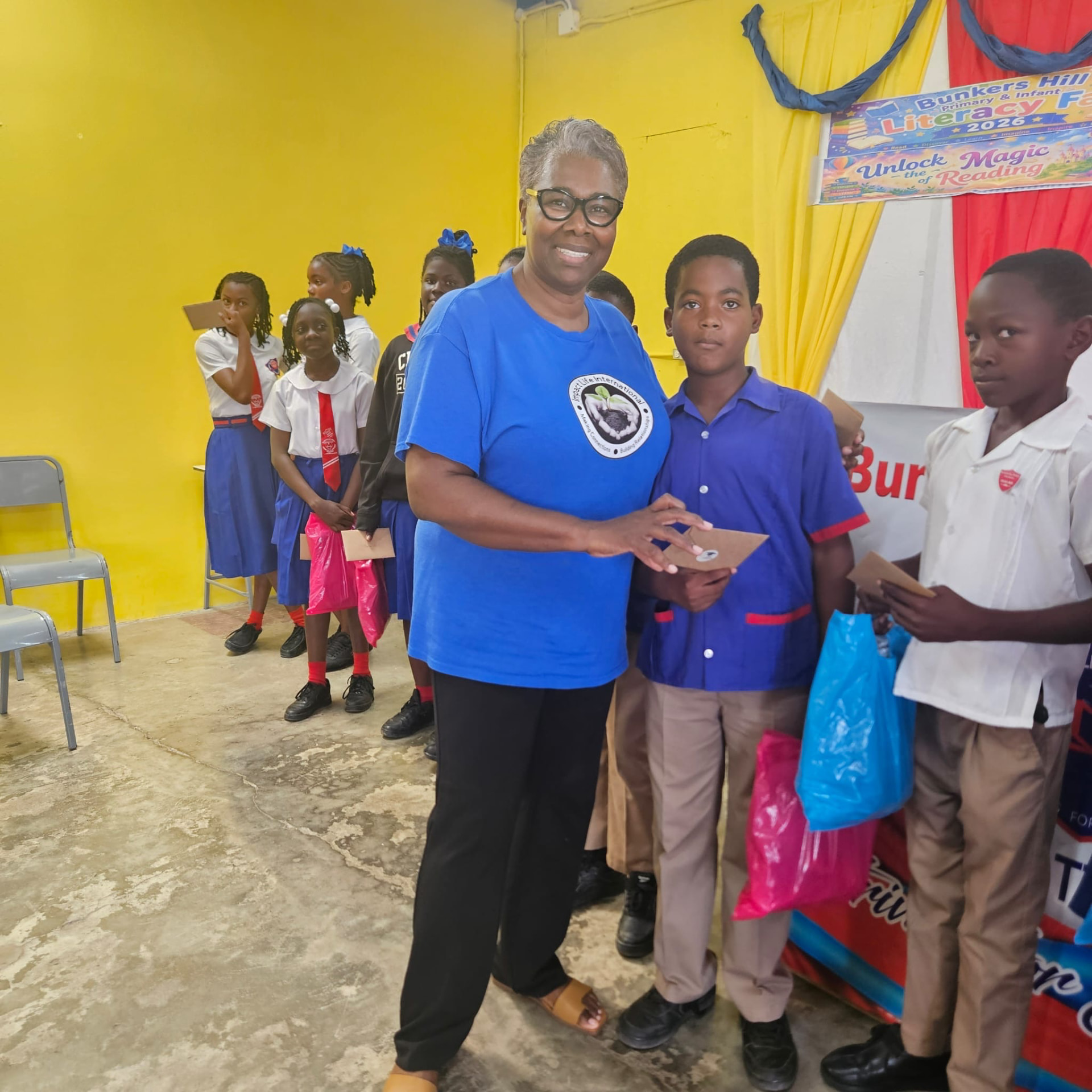 An Impact Life volunteer beside pupils holding envelopes and colorful bags at the literacy fair