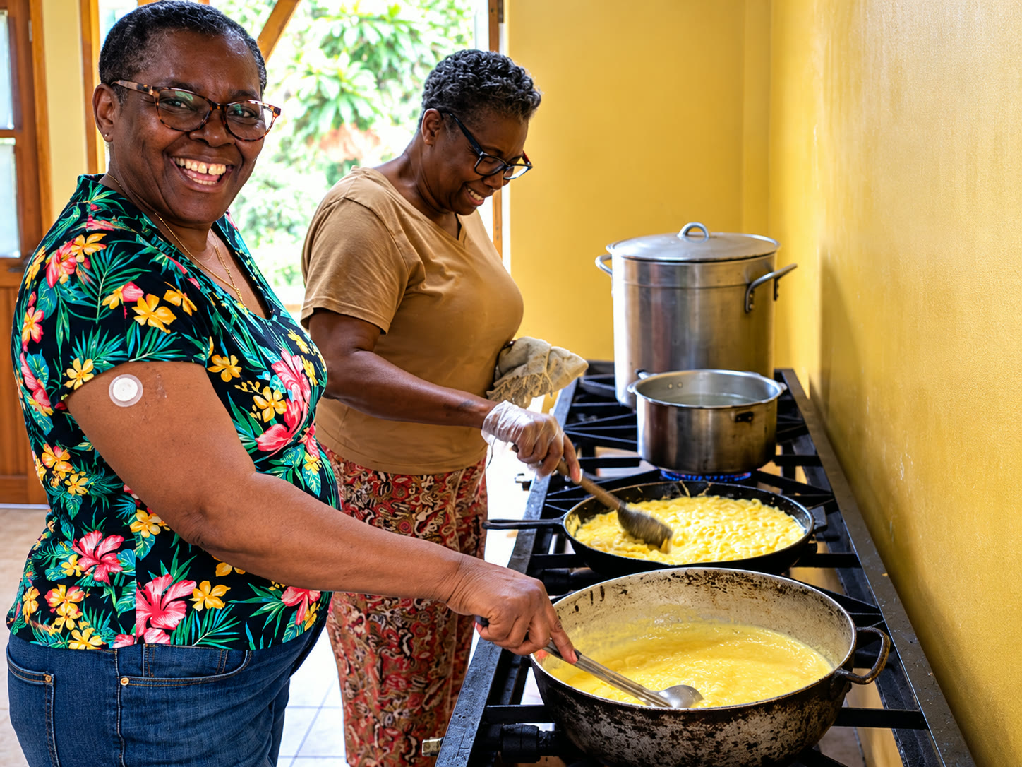 Two women standing at a commercial stove, stirring pots of food as they prepare a meal